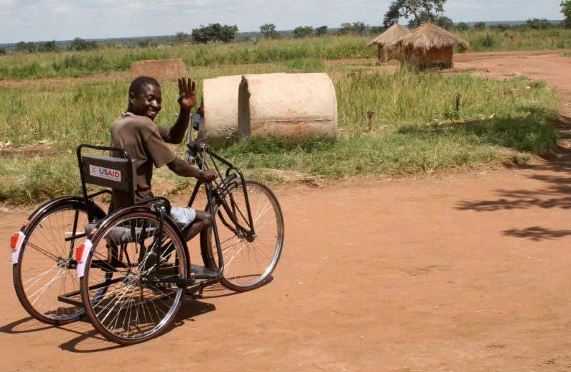 African man in a wheelchair waving to the camera.
