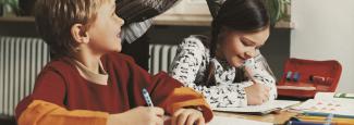 A girl and a boy studying with their teacher helping.