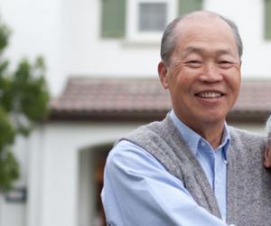 Older Asian couple embracing and posing for a picture in front of their home