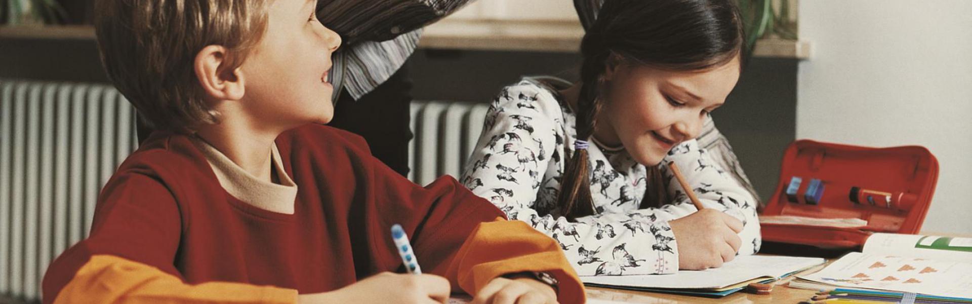 A girl and a boy studying with their teacher helping.